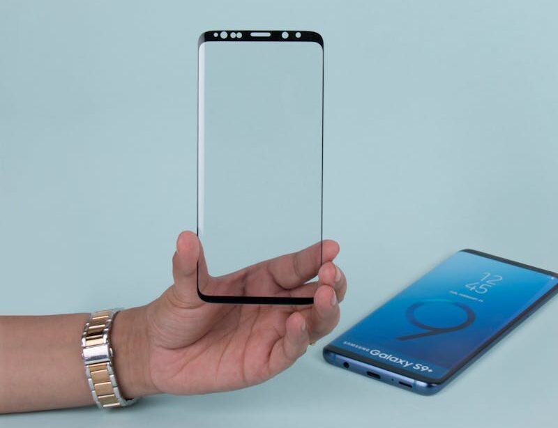 Close-up of a hand holding a transparent phone screen protector against a blue background.
